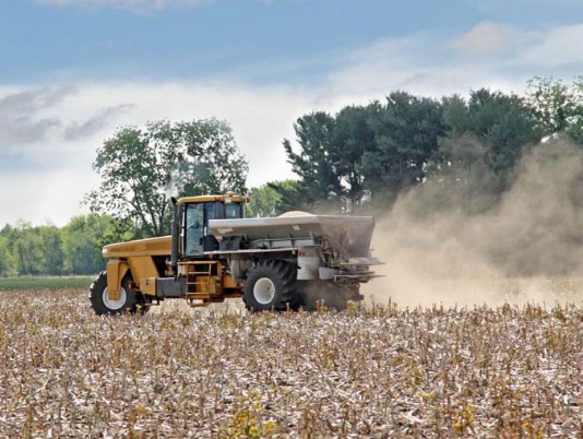 A tractor spreads lime on a crop field.