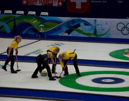 A curling team brushes the ice.