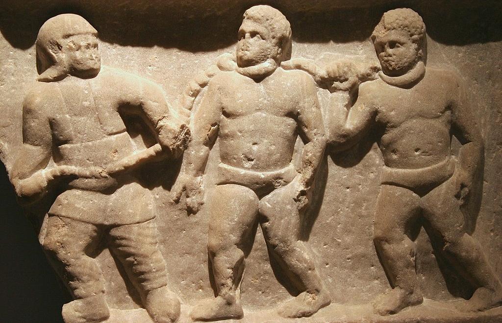 A Roman soldier leads slaves in collars linked by chains
